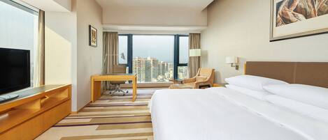 A hotel room with a large bed, a desk, a chair, a TV, and a view of the cityscape.