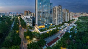 Un moderno hotel grattacielo con una facciata in vetro imponente, immerso nel verde e circondato da un paesaggio urbano curato.