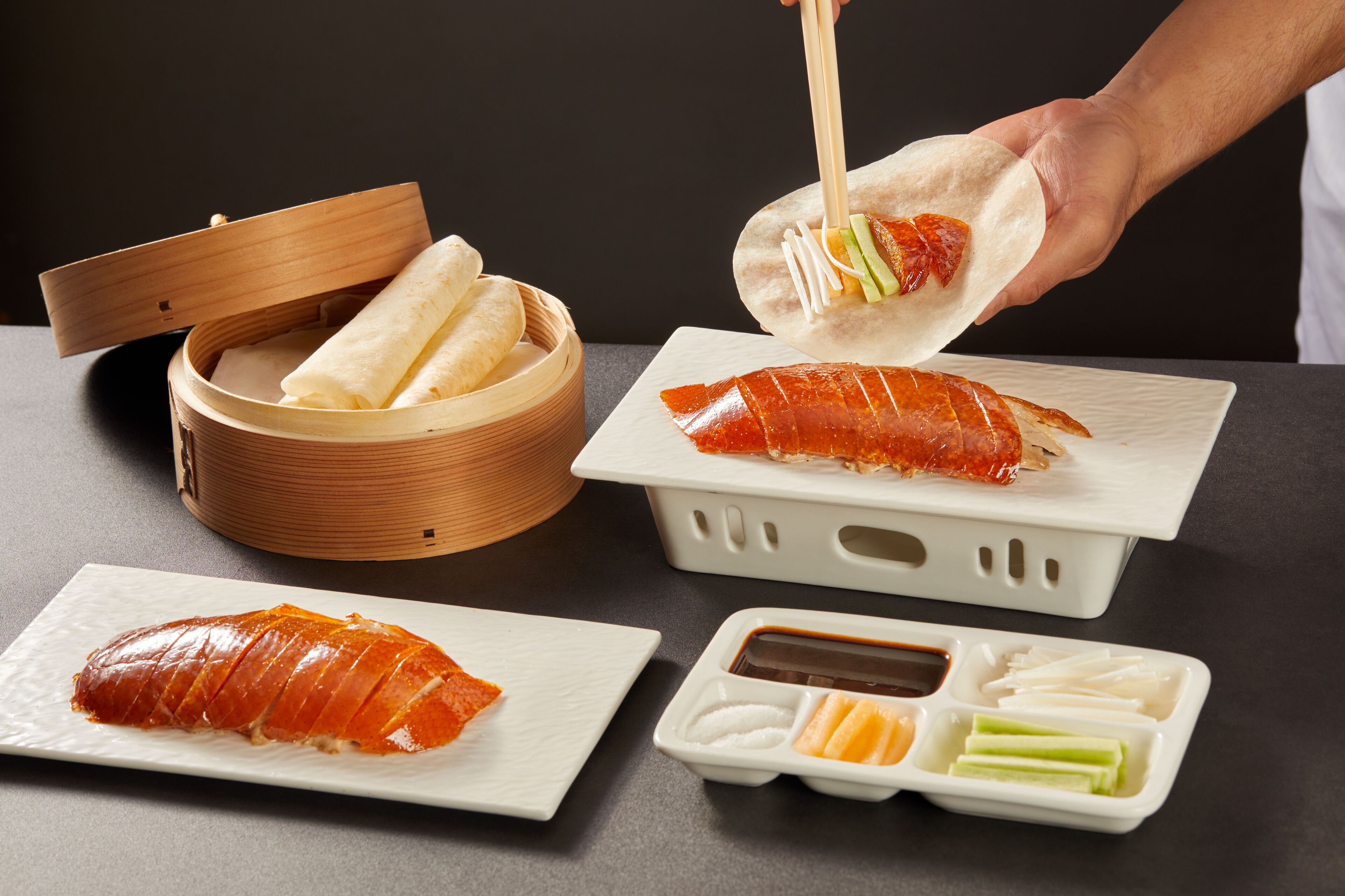 A sushi dish with a wooden container, a plate with a rolled fish, and a small dish with condiments.