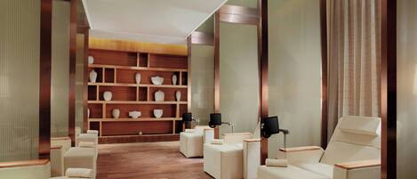 A modern spa room with wooden flooring, white seating, and a wall of decorative vases.