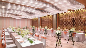 Salão de banquetes com longas mesas, toalhas brancas e arranjos florais.