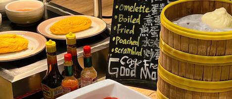 A breakfast buffet with omelettes, sauces, and a sign listing food options.