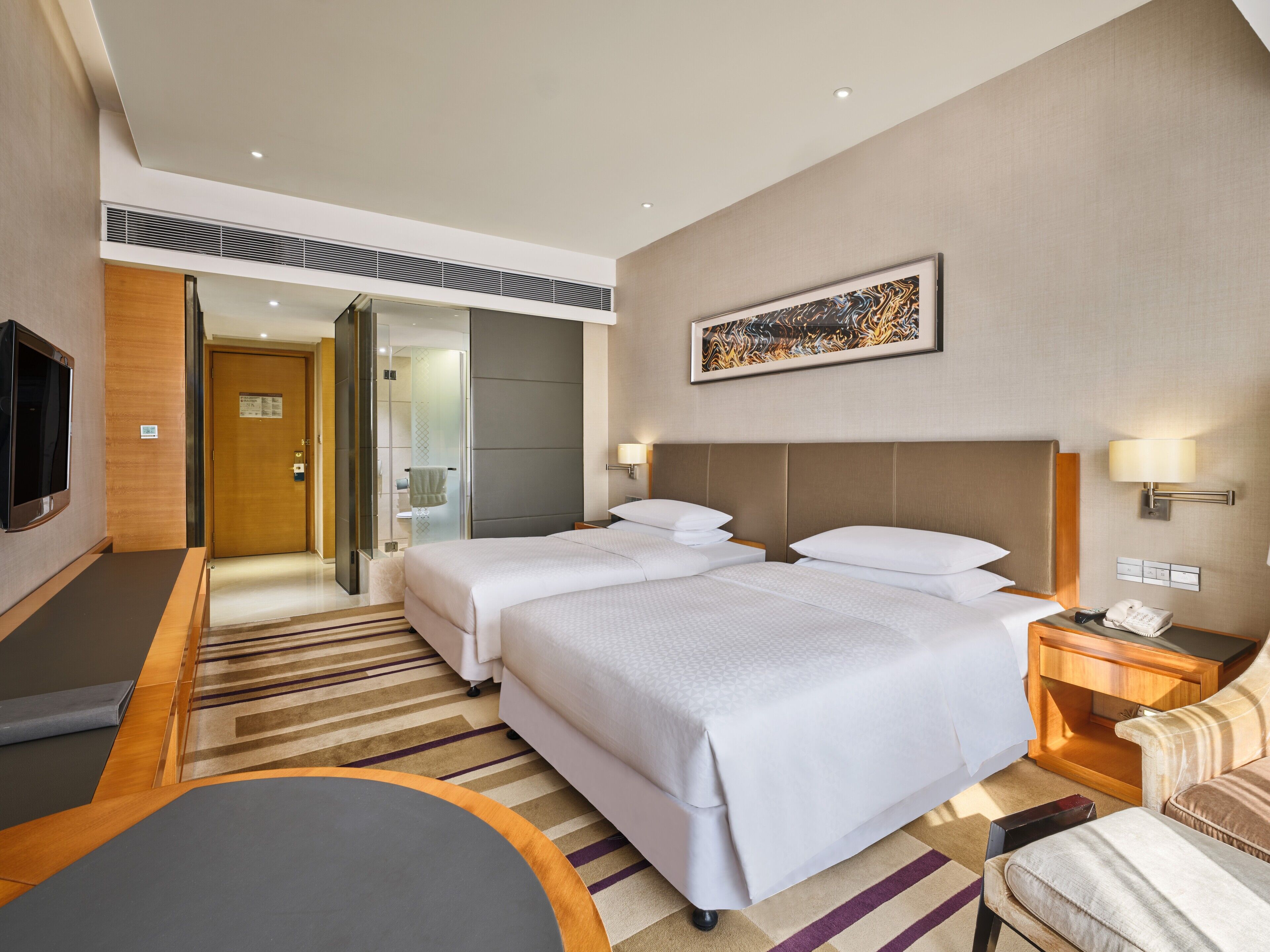 A hotel room with two beds, a TV, a desk, a chair, and a shower area.