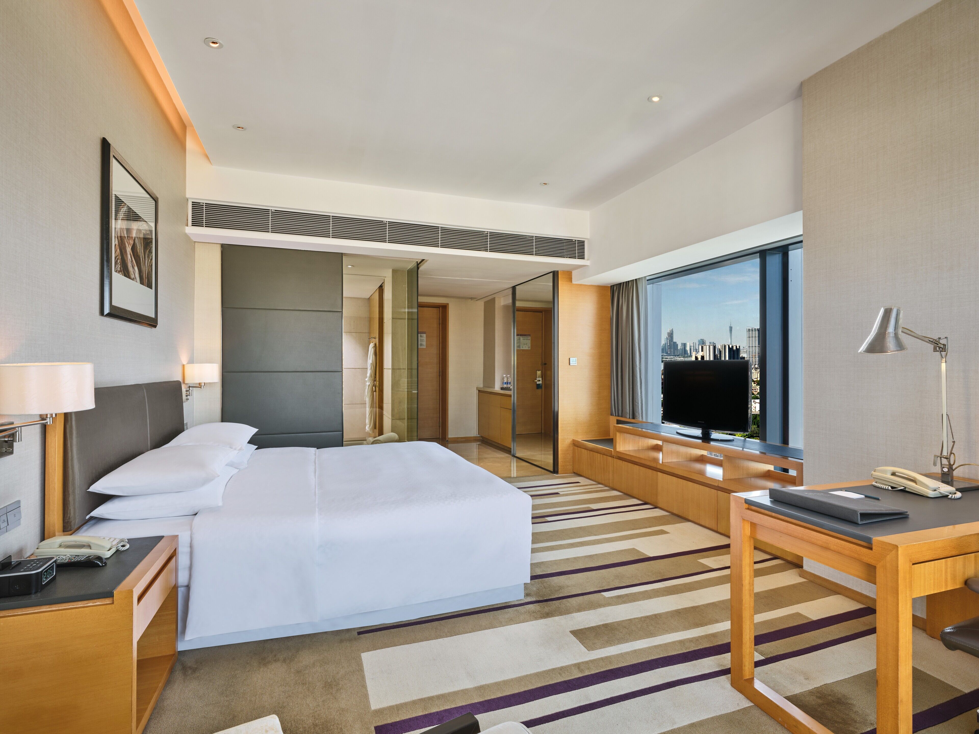 Una habitación de hotel con cama, escritorio, televisión y vistas al horizonte de la ciudad.