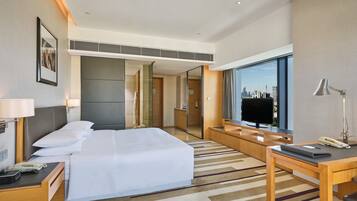 Una habitación de hotel con cama, escritorio, televisión y vistas al horizonte de la ciudad.
