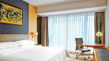 A hotel room with a large bed, a desk, a chair, a vase with flowers, and a painting on the wall.