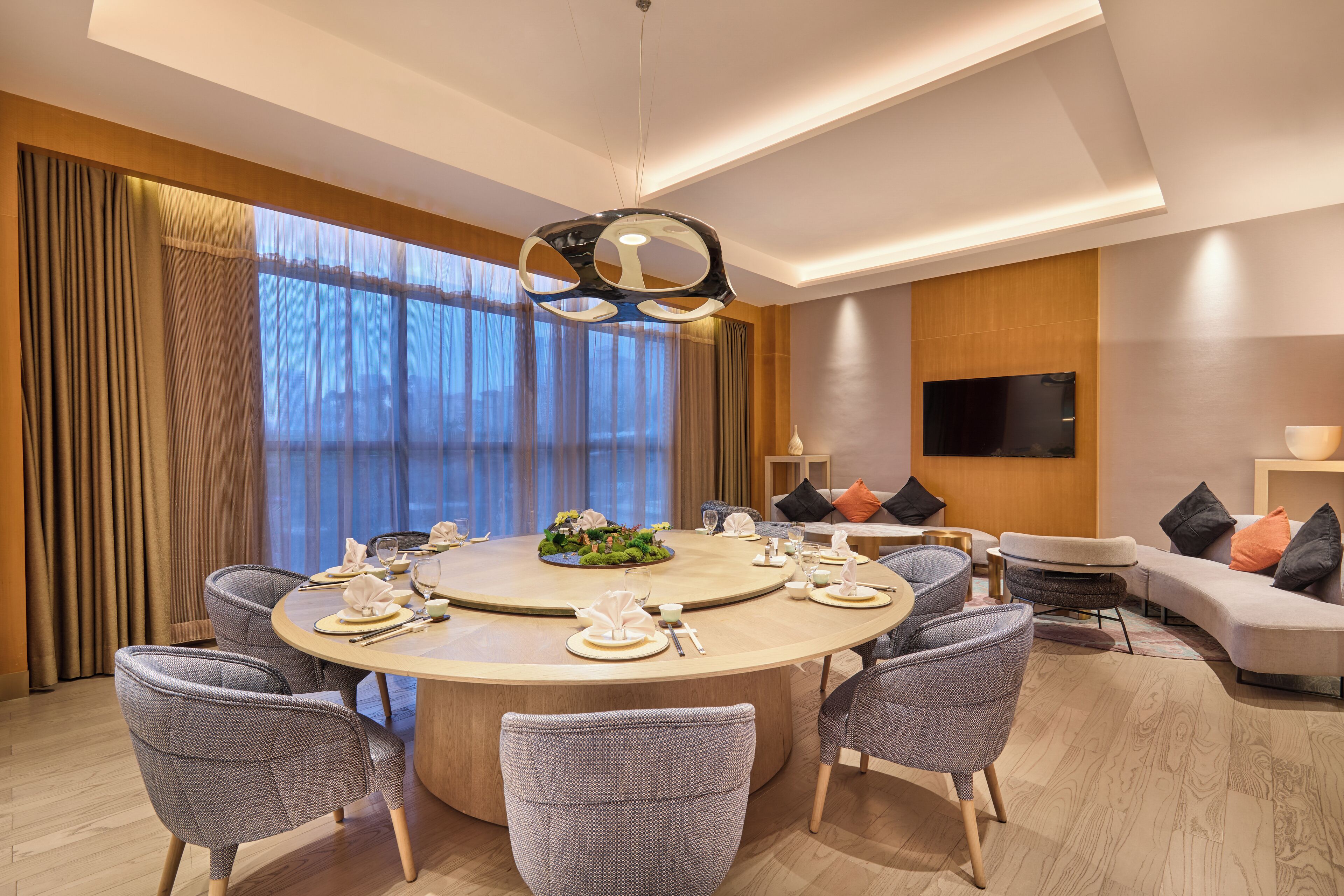 A modern dining area with a round table, chairs, and a central light fixture.