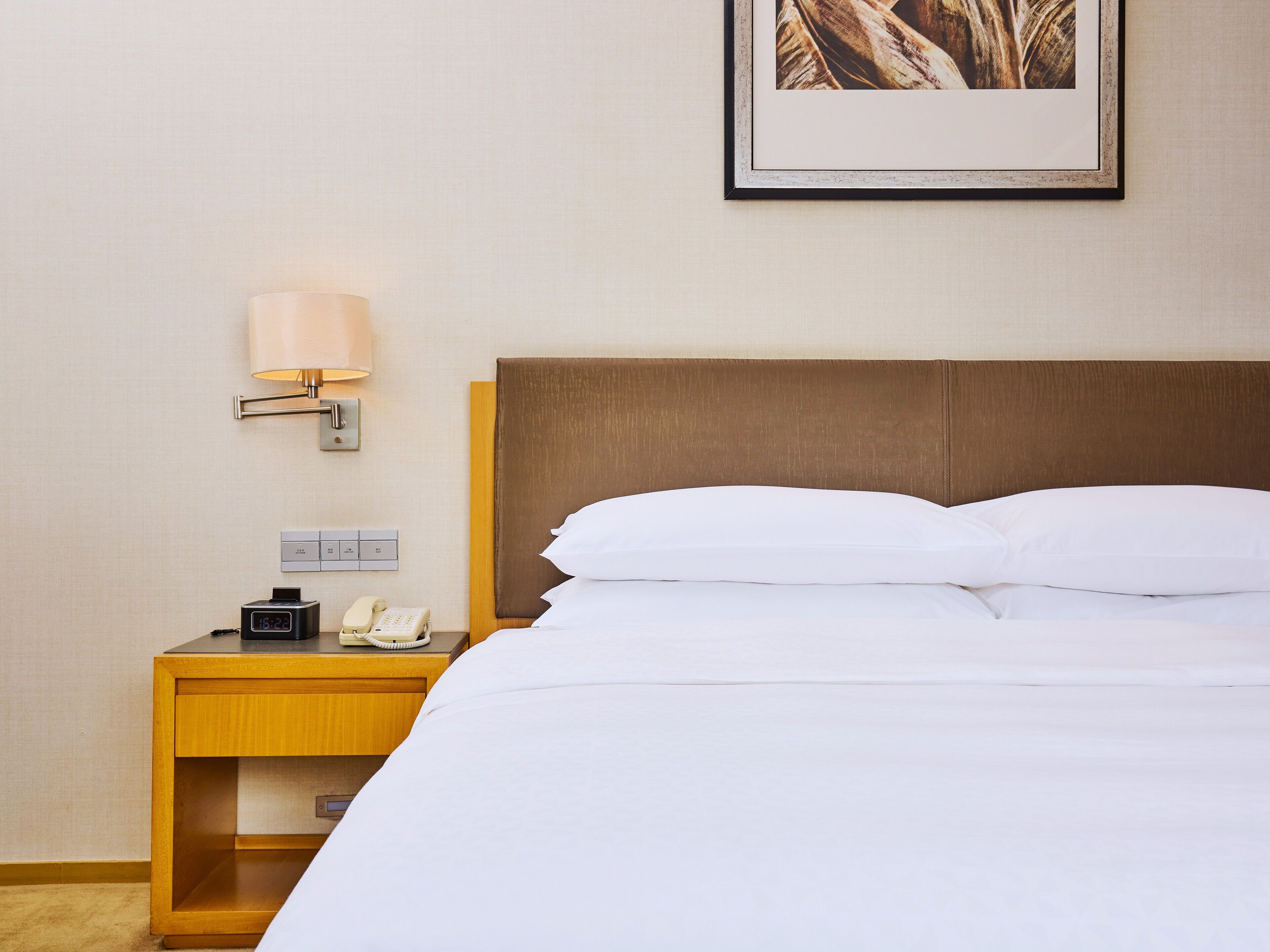 Une chambre d’hôtel comprenant un lit, une table de chevet, une lampe, un téléphone et un interrupteur fixé au mur.