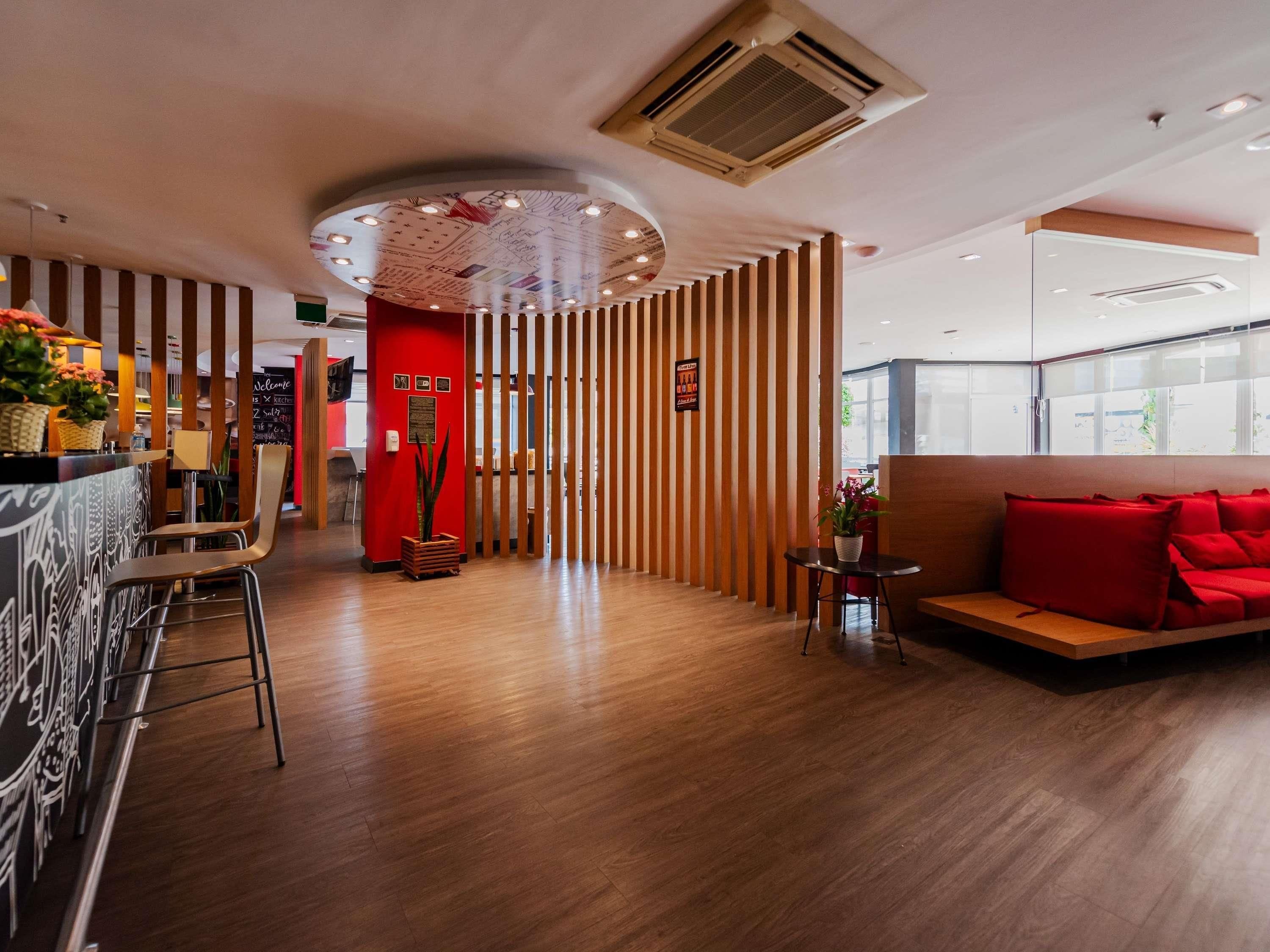 A modern hotel lobby with a wooden reception desk, seating area, and a red accent wall.