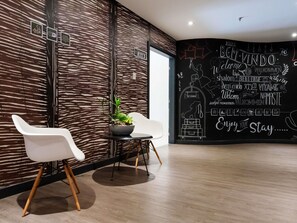 Un intérieur moderne avec un mur noir orné de messages d’accueil multilingues et une plante posée sur une table.