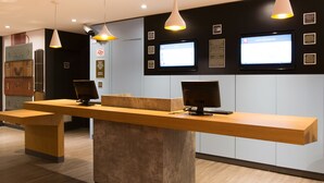 Un mostrador de recepción con dos monitores de ordenador, una encimera de madera e iluminación colgante.