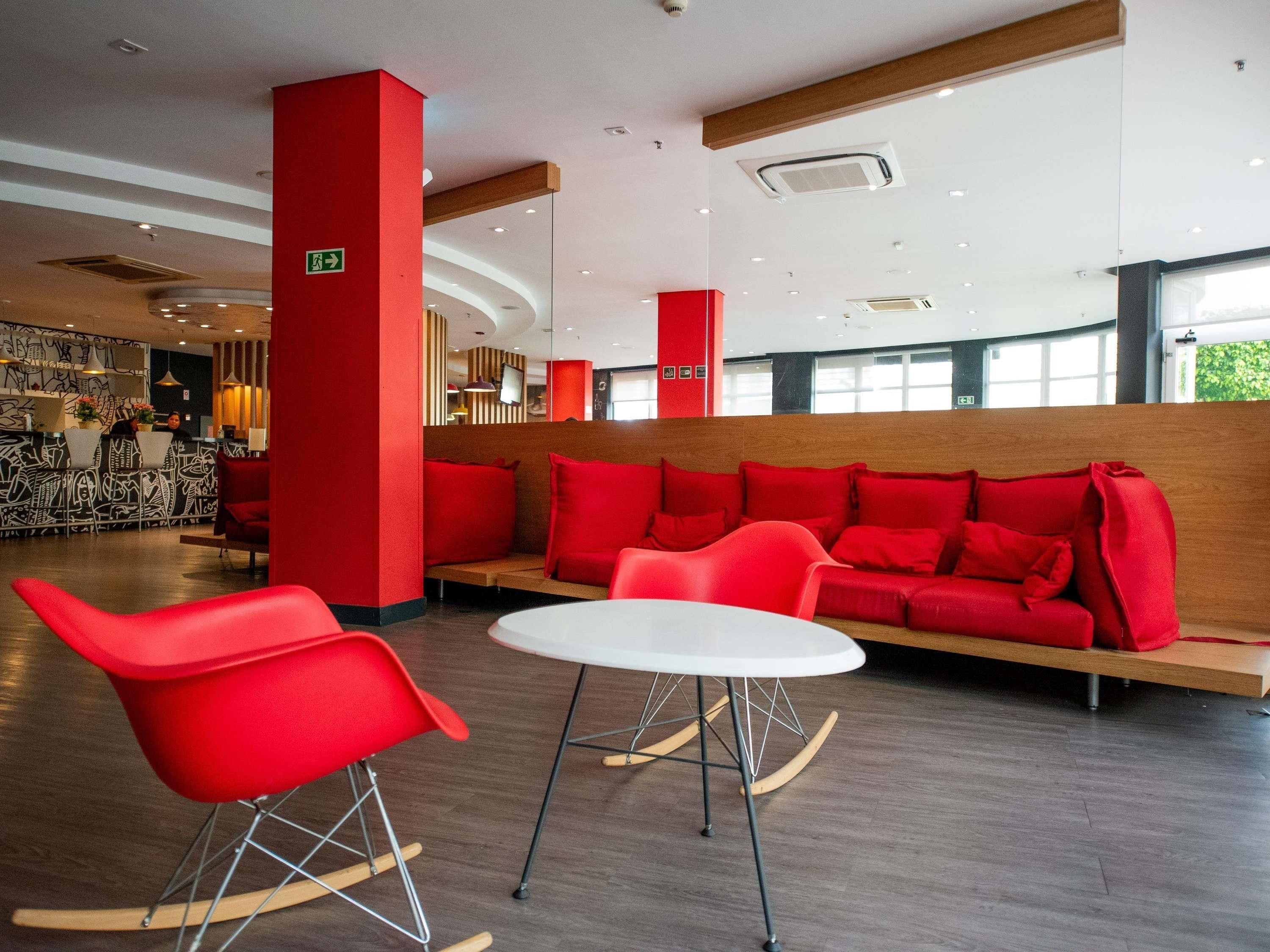 Un interior moderno con una zona de estar roja, una mesa blanca y un bar al fondo.