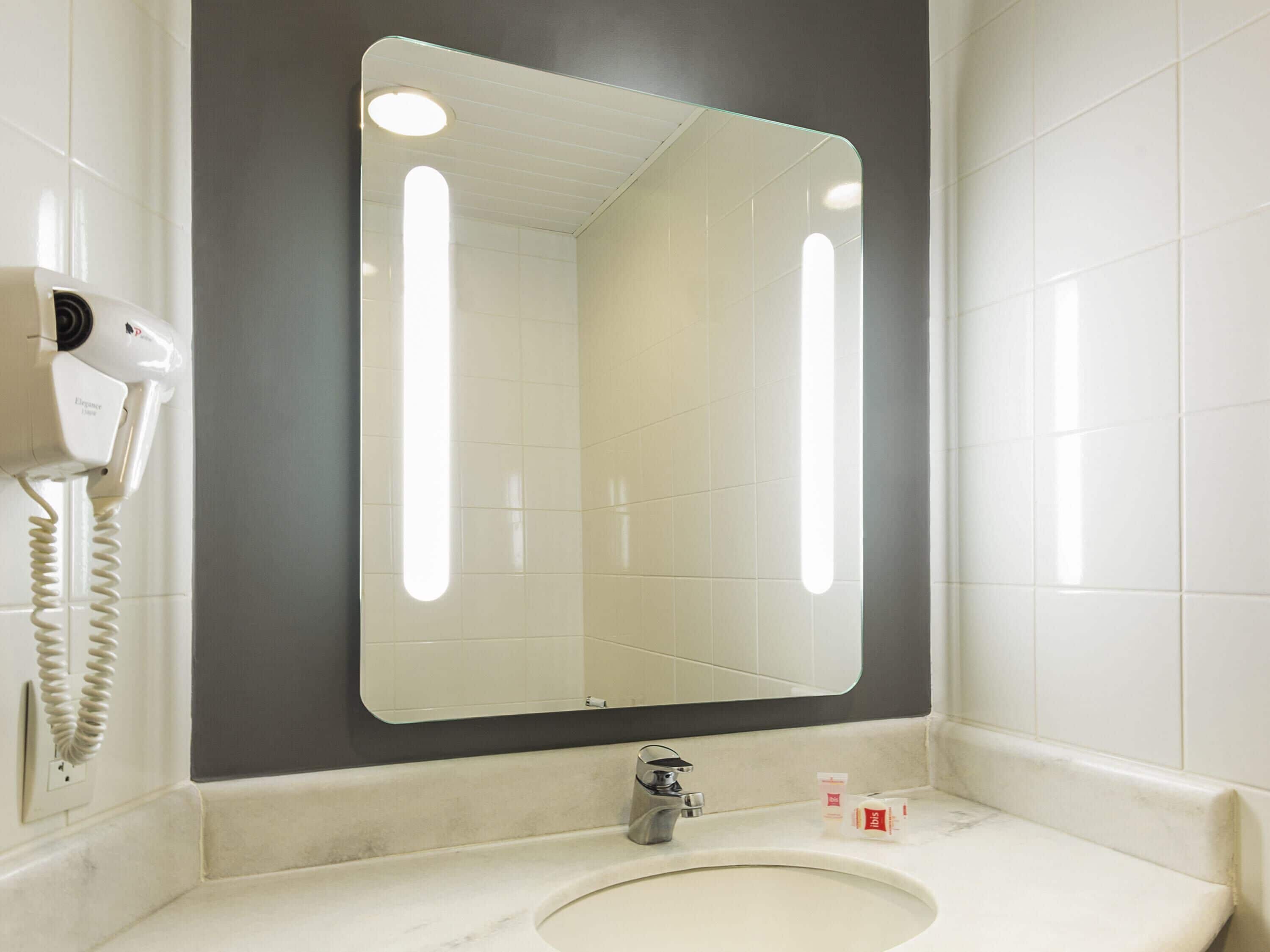 Un baño con un espejo grande, un secador de pelo y artículos de aseo en la encimera.