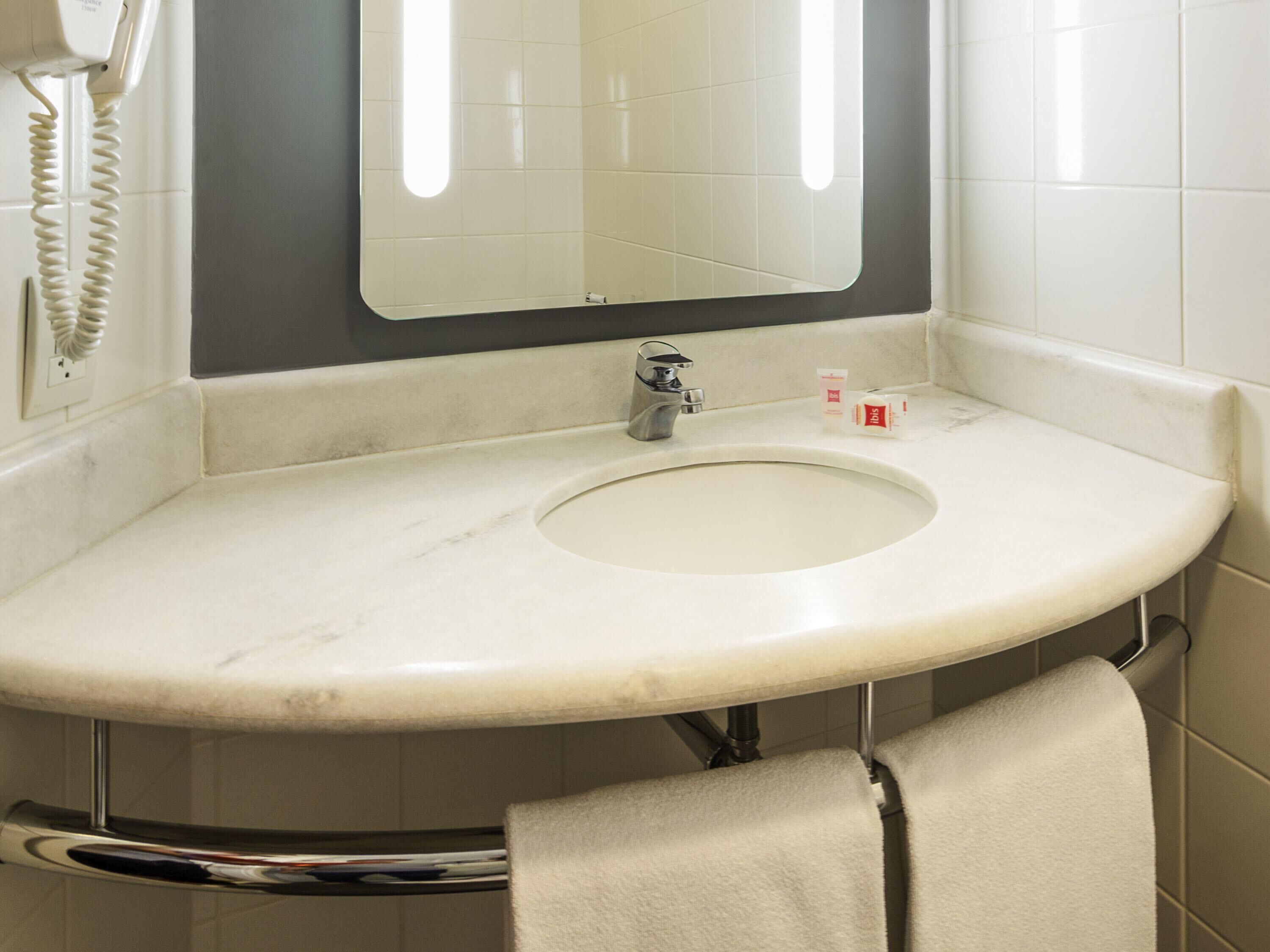 A bathroom with a white sink, a mirror, a towel rack, and a telephone.