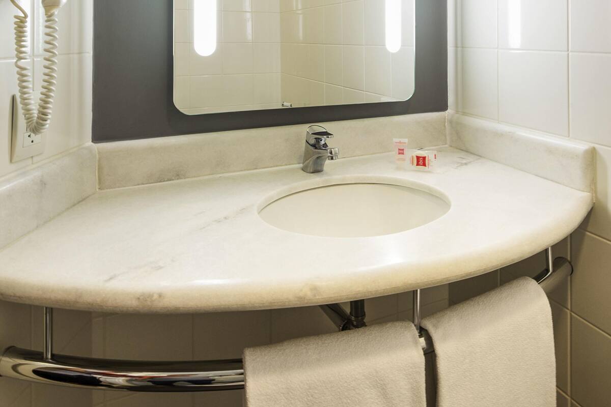 Un baño con un lavamanos blanco, un espejo, un perchero para toallas y un teléfono.