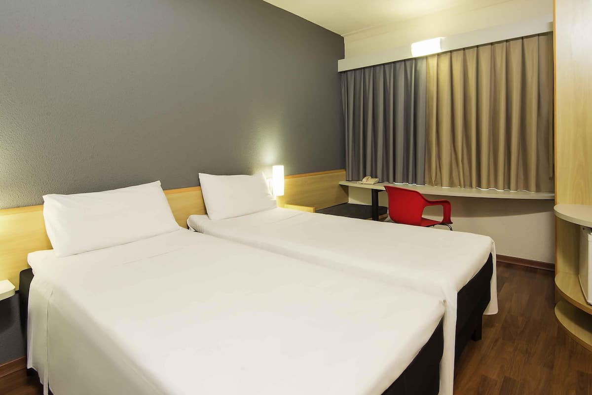 A hotel room with two beds, a desk, a chair, a telephone, and a window with curtains.