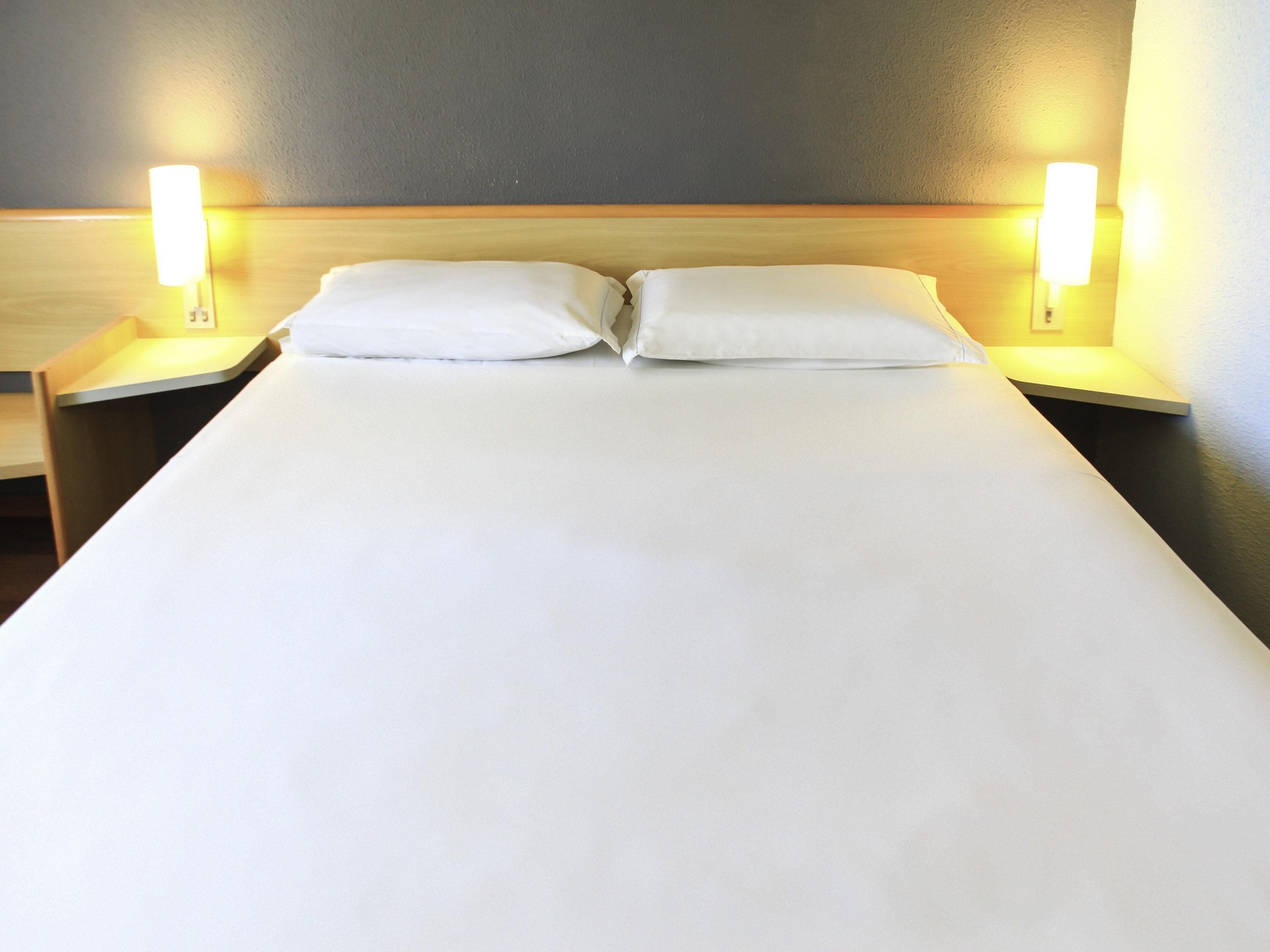 A hotel room with a large bed, two bedside lamps, and a plain wall.