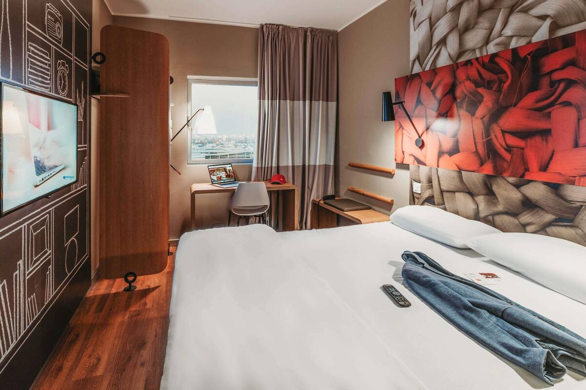 Ein Hotelzimmer mit Bett, Schreibtisch, Laptop, Fernseher und Blick auf die Stadt.
