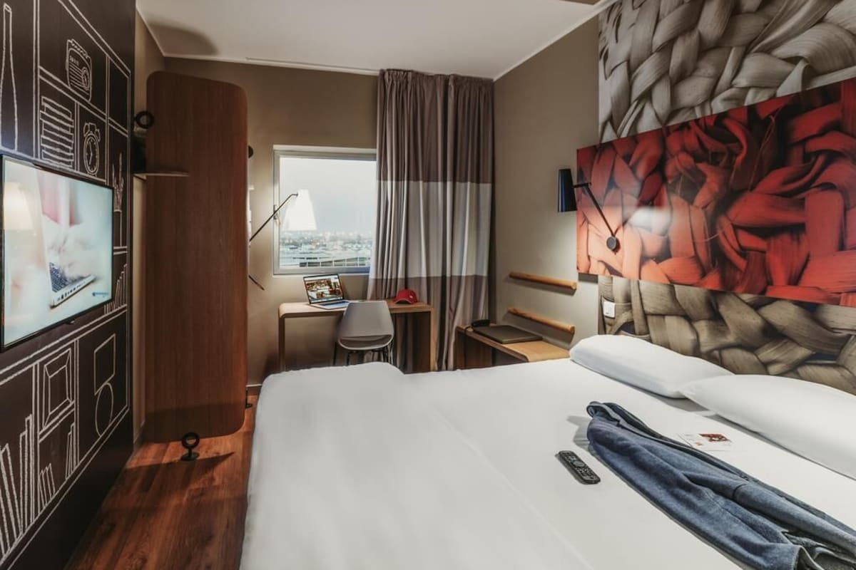 A hotel room with a bed, a desk, a TV, and a city view.