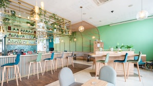 Una cafetería moderna con pared verde, barra de madera y varias zonas de estar.