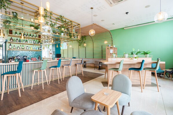A modern cafe with a green wall, wooden bar counter, and multiple seating areas.