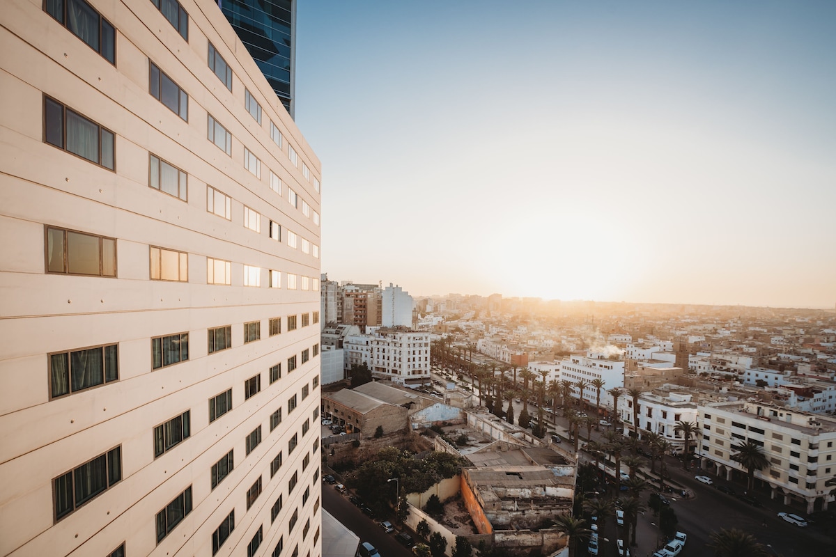 A high-rise building with multiple windows and a view of a cityscape during sunset.