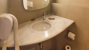 Un baño con lavamanos, espejo, dispensador de toallas y papel higiénico.