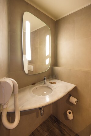 A bathroom with a sink, mirror, towel dispenser, and toilet paper.