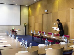 Une salle de conférence avec une longue table, des chaises, des bouteilles d’eau et un écran de projection.