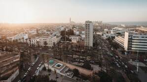 Vista aérea de un paisaje urbano con una torre destacada, una mezquita con cúpula verde y una calle concurrida con coches y palmeras.