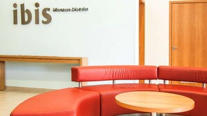 A red leather sofa and a small wooden table in a room with a white wall and a wooden door. - Ibis Manaus Distrito Industrial (Manaus)