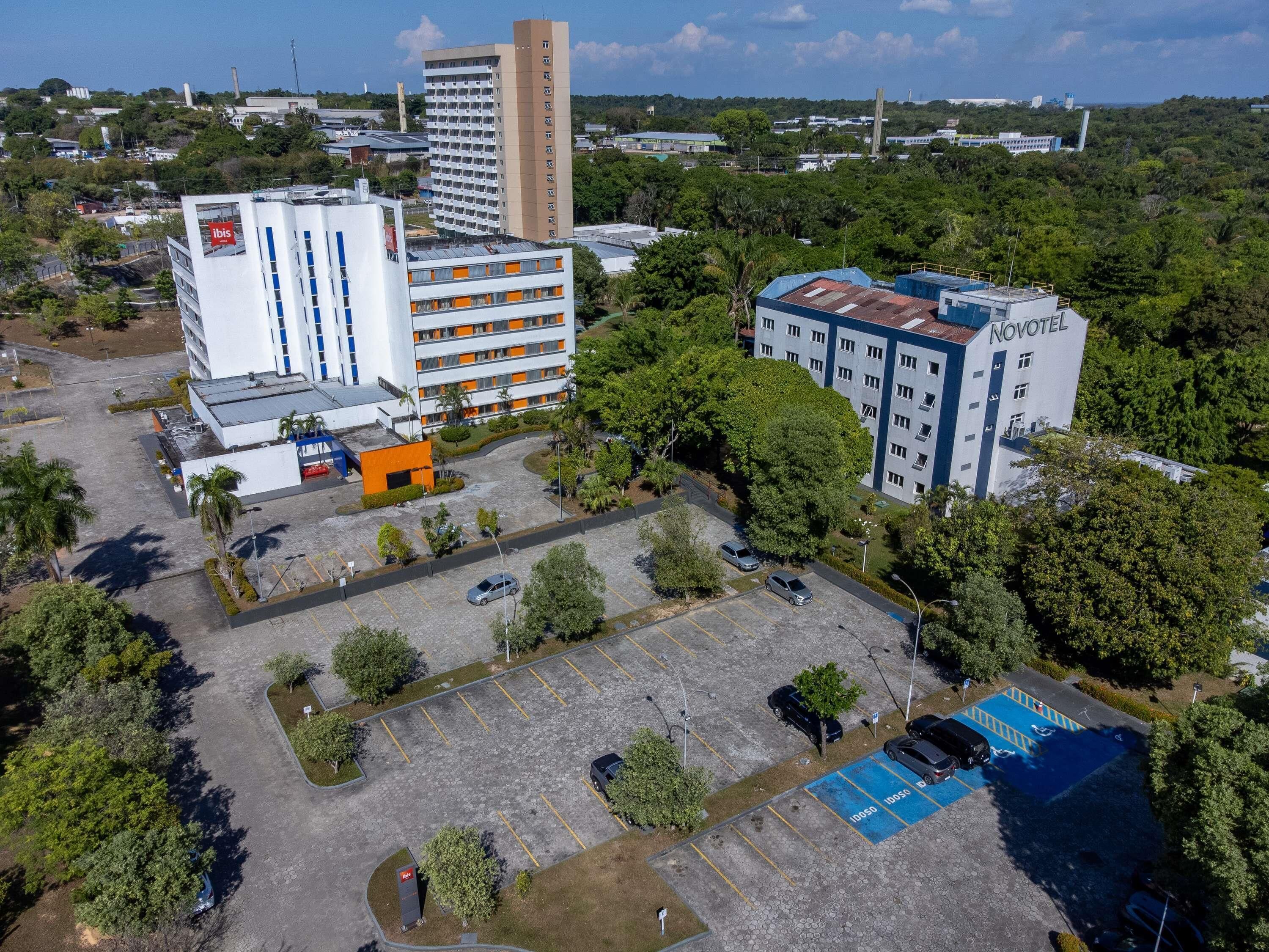 Vue aérienne d'un hôtel composé de plusieurs bâtiments, avec des zones de stationnement et une végétation luxuriante environnante.