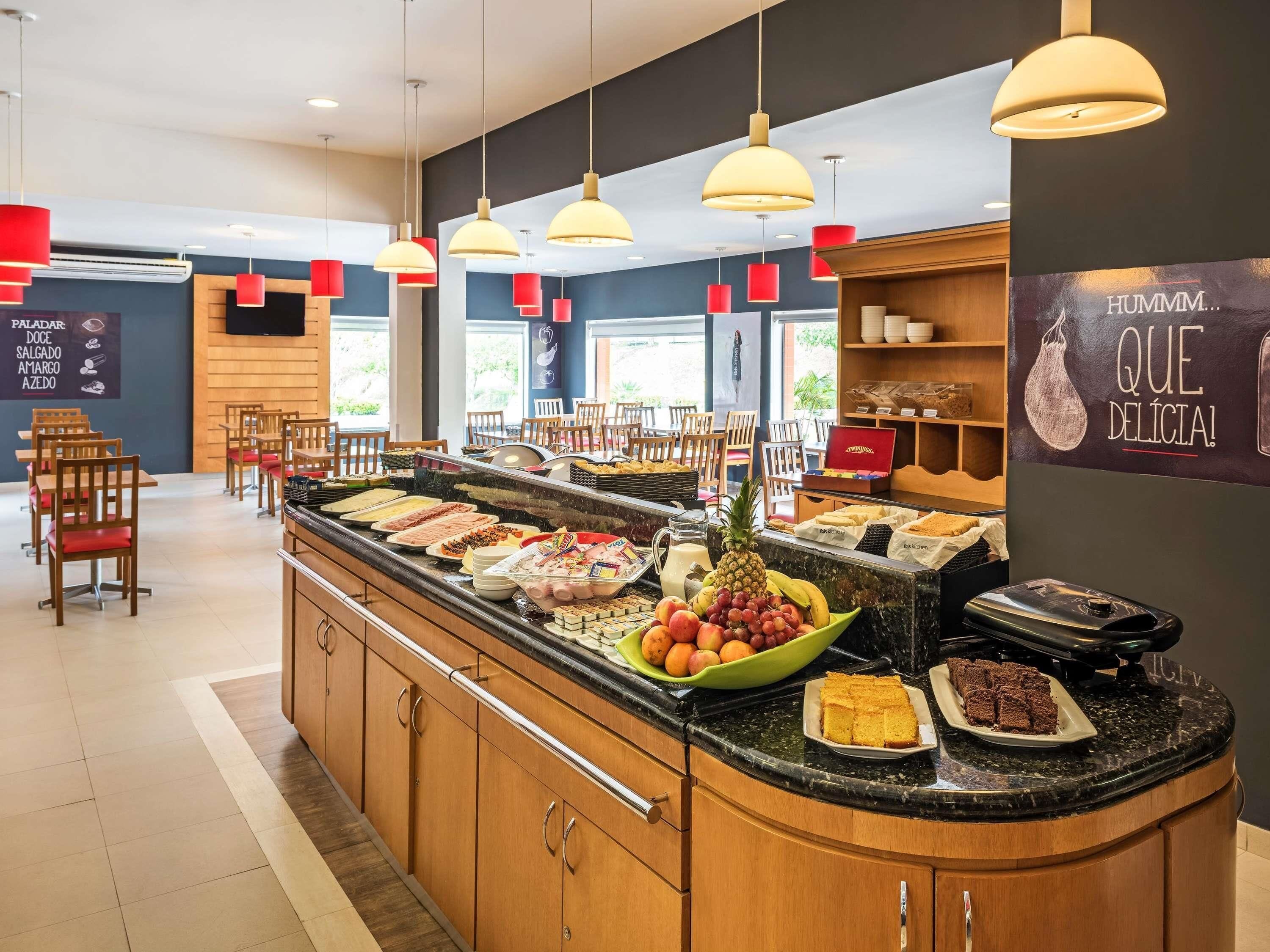 Un área de bufé con diversas opciones de comida, un espacio de asientos con sillas y una barra con exhibición de productos horneados.