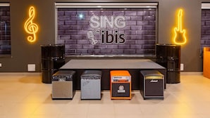 A stage with a neon sign reading "SING on ibis" and four amplifiers in front. - Ibis Manaus Distrito Industrial (Manaus)