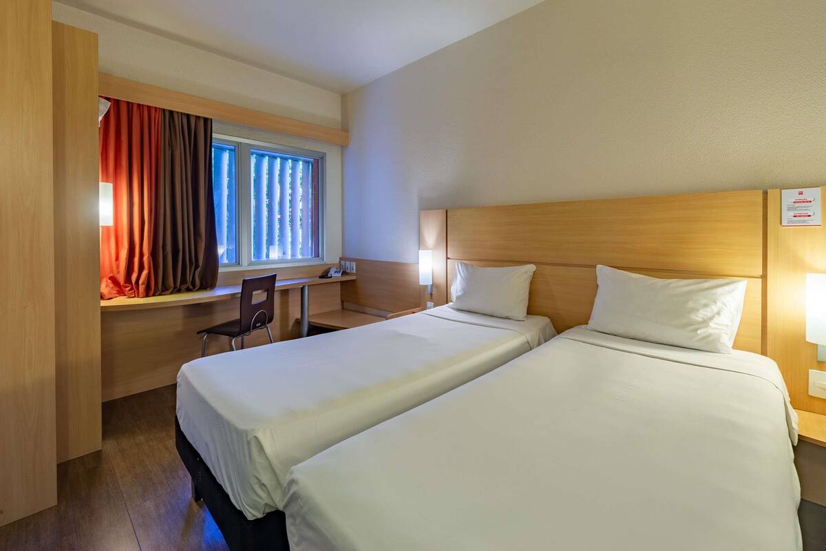 A hotel room with two beds, a desk, and a chair.