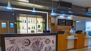 A modern bar area with a counter, shelves of liquor bottles, and a person behind the counter. - Ibis Manaus Distrito Industrial (Manaus)