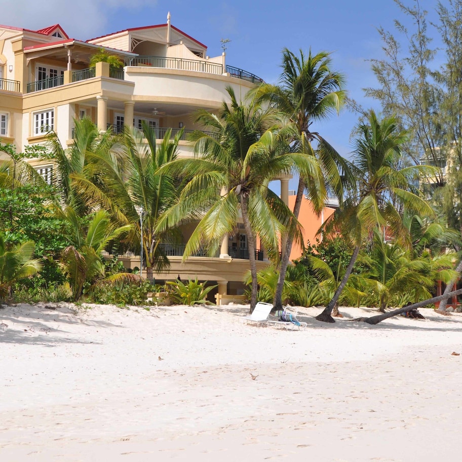 A beachfront property with a multi-story building, palm trees, and a sandy beach.