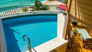 A swimming pool with a view of the ocean, a beach, and a patio area with chairs and a table. - White Sands Beach Condos (St. Lawrence Gap)