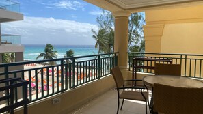 A balcony with a view of the ocean, a table, and chairs. - White Sands Beach Condos (St. Lawrence Gap)