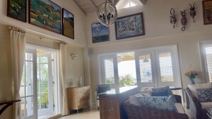 A spacious living room with large windows, a chandelier, and artwork on the walls. - White Sands Beach Condos (St. Lawrence Gap)