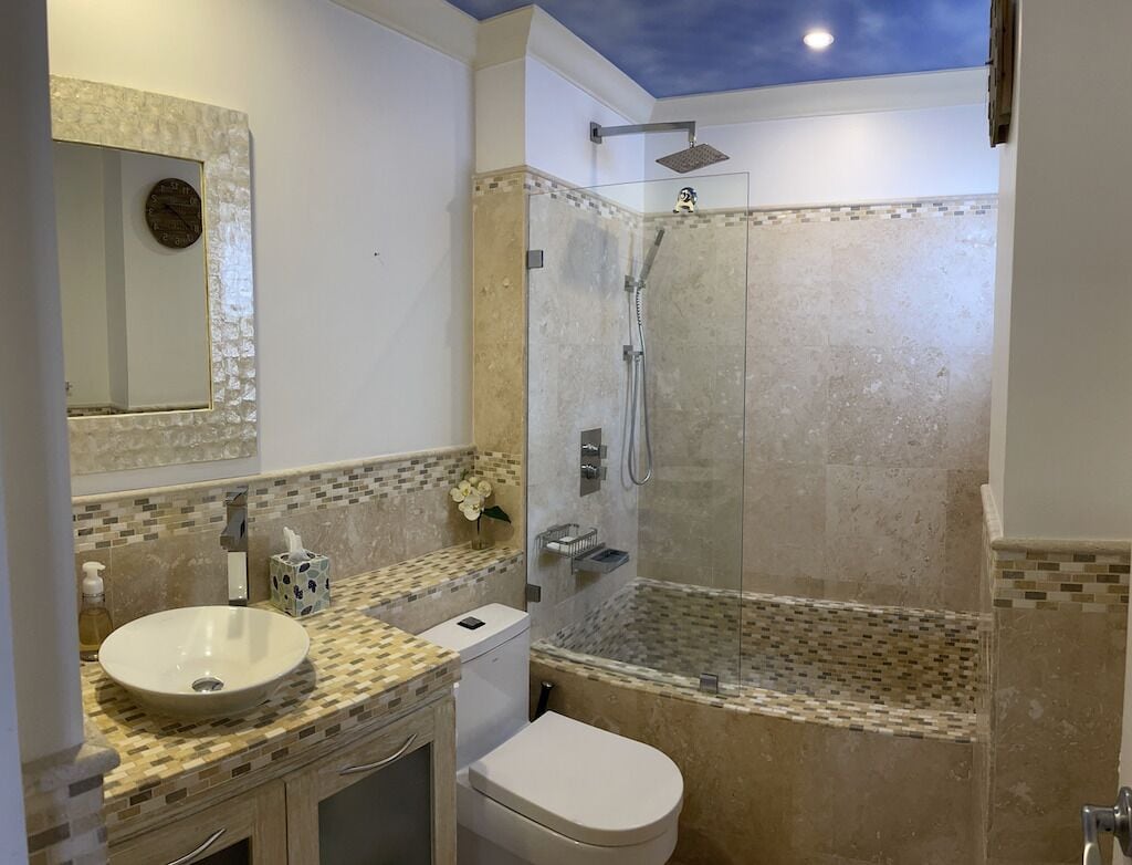 A bathroom with a glass-enclosed shower, a sink with a mosaic tile backsplash, and a toilet.