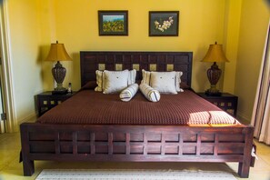A large bed with a wooden headboard, two bedside tables with lamps, and two framed pictures on the wall. - White Sands Beach Condos (St. Lawrence Gap)