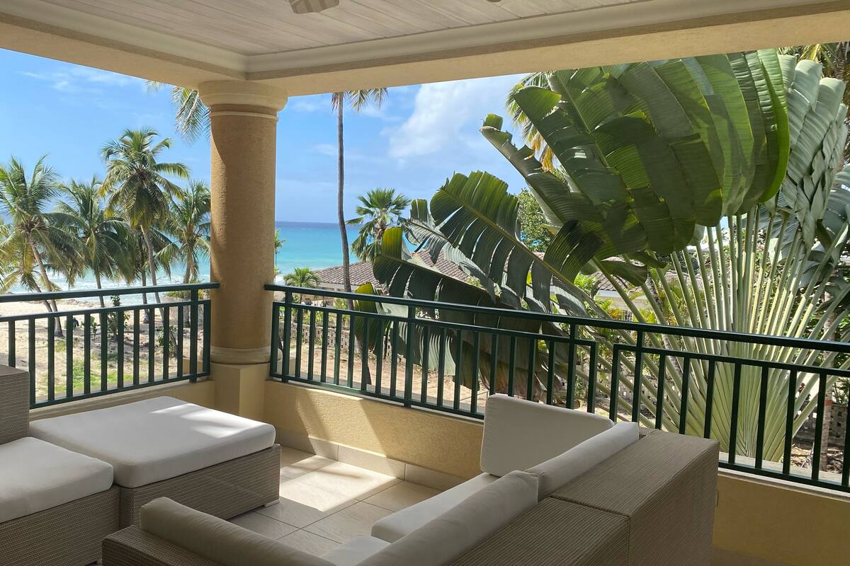 Een balkon met rieten meubilair en uitzicht op het strand en palmbomen.