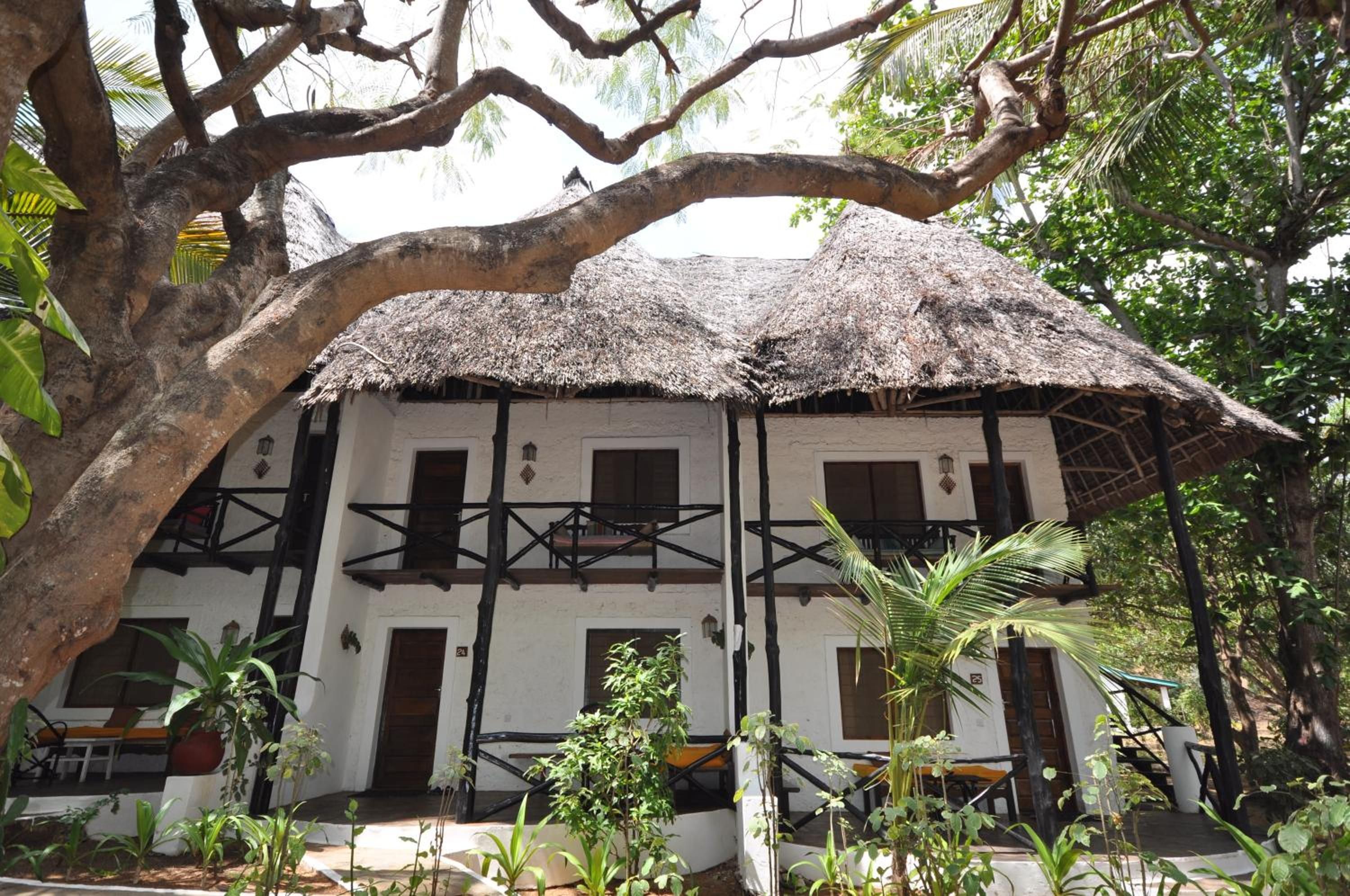 A two-story building with a thatched roof, surrounded by lush greenery.