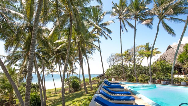 A poolside area with lounge chairs, palm trees, and a view of the ocean. - Baobab Sea Lodge (Kilifi)