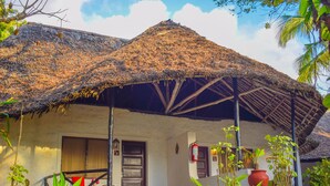 A traditional thatched-roof house with a wooden door and windows, surrounded by lush greenery. - Baobab Sea Lodge (Kilifi)