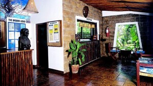 A reception area with a wooden ceiling, a reception desk, a wall-mounted sign for 'The Brobaab Lodge', a reception desk with a plant, and a window with a view of greenery. - Baobab Sea Lodge (Kilifi)