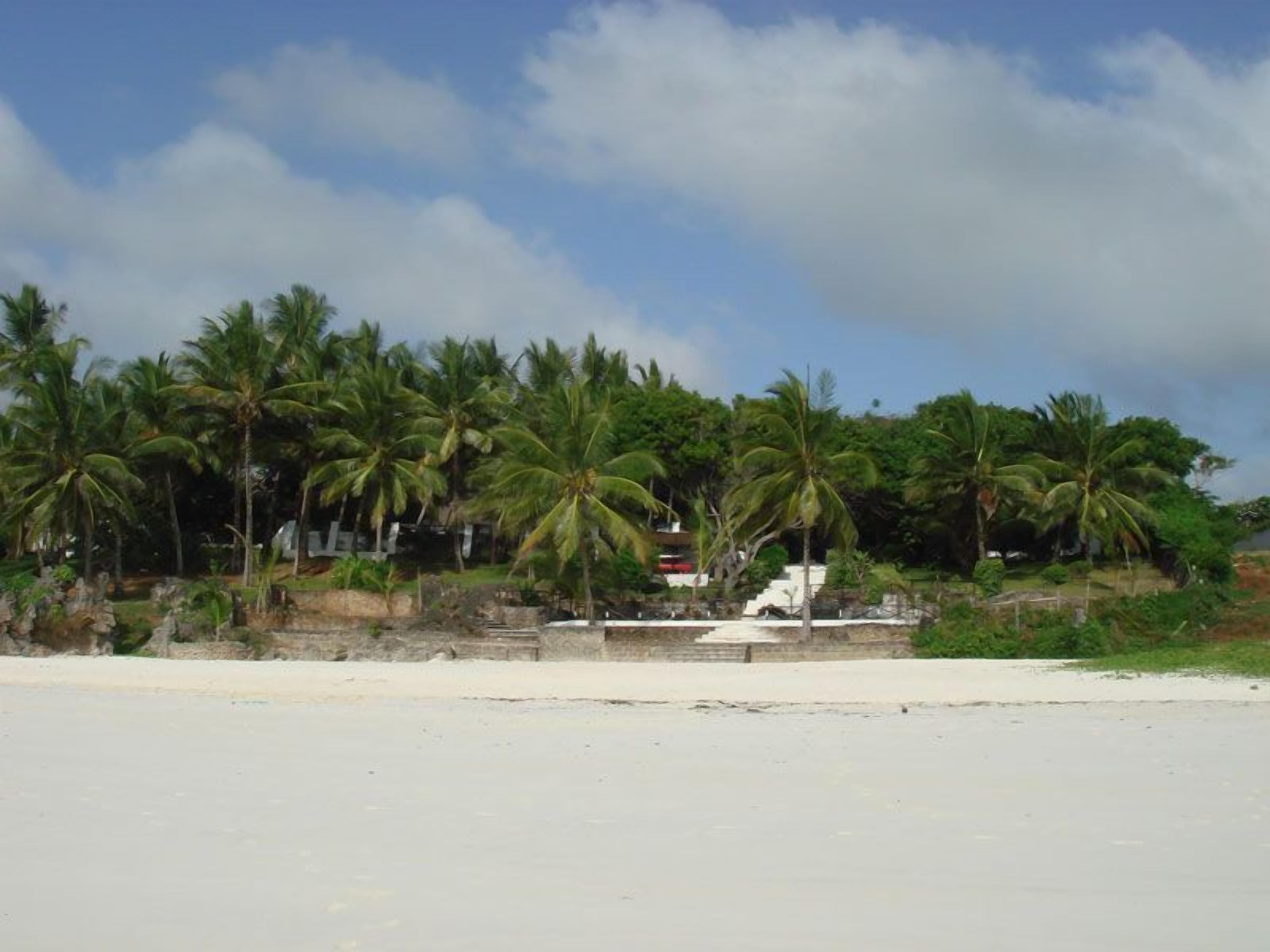 A beach with palm trees and a white building in the background.