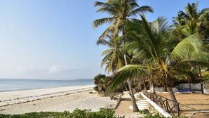 A beach with palm trees, a sandy path, and a beach chair. - Baobab Sea Lodge (Kilifi)