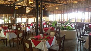 Un restaurante con mesas dispuestas para comer, sillas de madera y un tejado de paja.